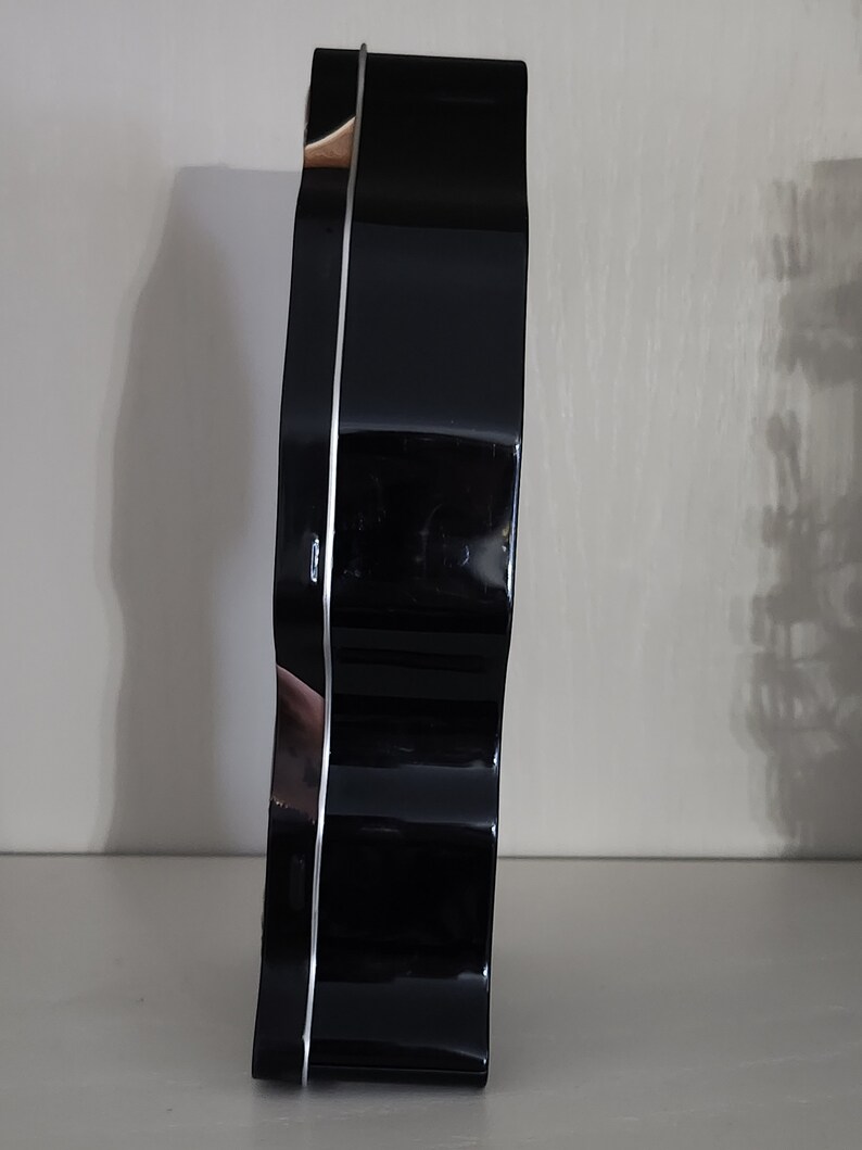 Puede incluir: Una lata de galletas de metal negro con un dise&ntilde;o de borde ondulado. La lata tiene un borde plateado.
