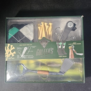 May include: A golf-themed gift set in a clear box. It includes golf tees, a multi-tool kit, crew socks, and a bottle opener. The socks have a green and black argyle pattern. The multi-tool kit includes a magnetic ball marker, club groove brush, and a divot tool.