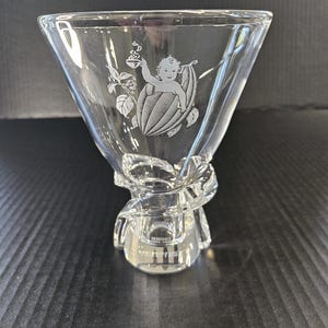 May include: A clear glass vase with a twisted stem and a decorative etched design of a cherub holding a cup. The cherub is sitting inside a gourd.