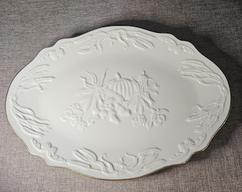 May include: White oval serving platter with a raised design of wheat stalks and a pumpkin with grapes. The platter has a gold rim.