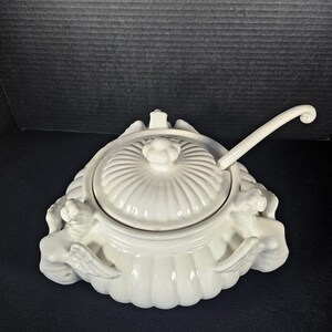 May include: White ceramic soup tureen with angel wing handles and a lid. The tureen has a fluted design and comes with a matching ladle.
