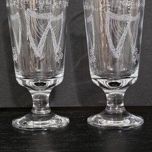 May include: Two clear glass goblets with a stem and a wide base. The goblets are etched with the words "Coffee Irish Coffee" and a design of a harp.