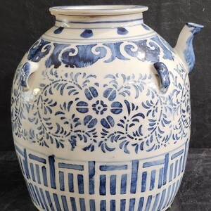 May include: A white ceramic jar with a blue and white floral design. The jar has two handles and a spout. The jar is decorated with a blue and white geometric pattern at the bottom.