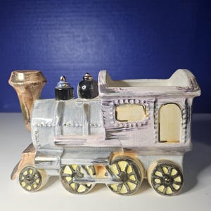 May include: A vintage ceramic train planter in shades of gray, pink, and brown with gold accents. The train has a detailed design with wheels, a smokestack, and a caboose.