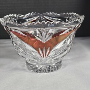 May include: A clear crystal bowl with a scalloped rim and a decorative base. The bowl features a red and gold design on the interior, with a cut glass pattern. The bowl is likely used for decorative purposes.