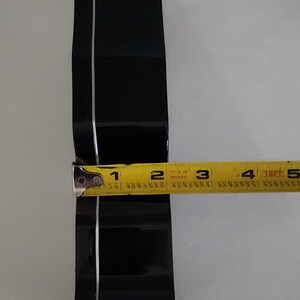 Puede incluir: Un cortador de galletas de metal negro en forma de coraz&oacute;n, medido con una cinta m&eacute;trica amarilla de aproximadamente 7,6 cm de ancho.