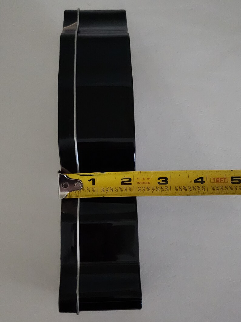 Puede incluir: Un cortador de galletas de metal negro en forma de coraz&oacute;n, medido con una cinta m&eacute;trica amarilla de aproximadamente 7,6 cm de ancho.