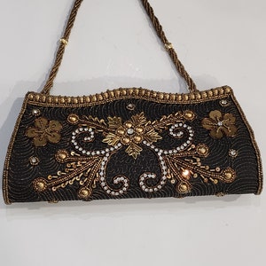 May include: A black beaded clutch bag with a gold chain strap and intricate gold and crystal embellishments.