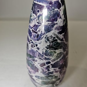 May include: A tall, decorative vase with a unique, abstract design. The vase features a blend of purple, blue, and white colors, creating a marbled effect. The top has a distinctive, curved shape. This ceramic vase is suitable for home decor.