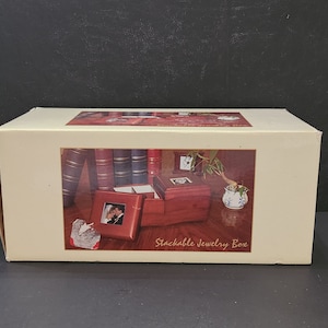 May include: A cream-colored box with an image of a stackable jewelry box. The jewelry box is open, revealing a photo frame and a small plant. The box has the words "Stackable Jewelry Box" printed on it.