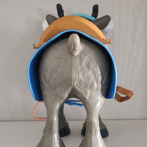 Pu&ograve; includere: Figura di renna giocattolo, vista da dietro, con sella e imbracatura. La figura &egrave; principalmente grigia con zoccoli e corna neri. La sella &egrave; arancione e blu, con cinghie marroni. Il giocattolo &egrave; progettato per bambini.