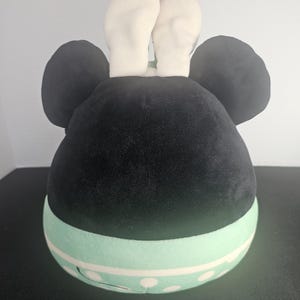 May include: A plush toy shaped like a character's head, featuring large black ears and white bunny ears. The base is light green with white polka dots. The toy is designed to resemble a popular cartoon character.
