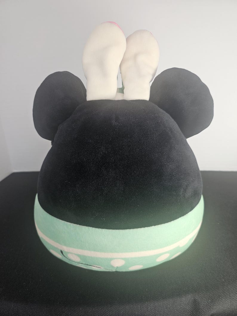 May include: A plush toy shaped like a character's head, featuring large black ears and white bunny ears. The base is light green with white polka dots. The toy is designed to resemble a popular cartoon character.