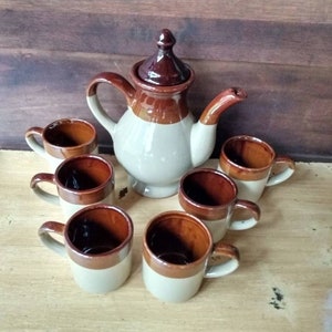 May include: A set of six brown and beige ceramic mugs with a brown and beige ceramic teapot with a lid.