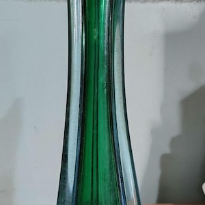 May include: A tall, slender, vintage glass vase with a flared base and a narrow neck. The vase is primarily green with blue accents and a label near the base. The vase is approximately 12 inches tall.