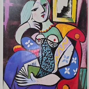 May include: A framed print of a cubist artwork featuring a seated figure. The figure has a green face, blue dress, and holds a fan. The chair is red and yellow, with a framed profile in the background. The artwork is in a black frame.