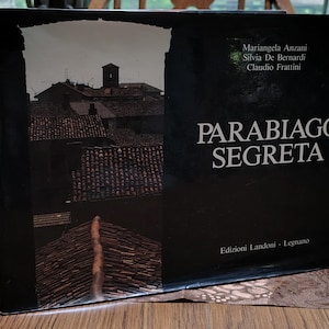 May include: A hardcover book titled "Parabiago Segreta" with a dark cover featuring a rooftop scene. The book's title is in large white letters, with author names above and publisher information below.