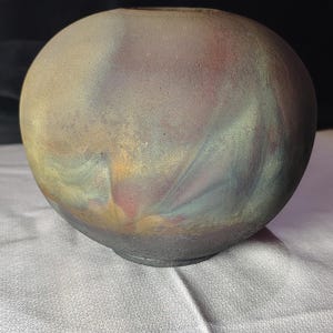 May include: A spherical ceramic vase with a textured, matte finish. The surface features a blended color palette of muted earth tones, including charcoal gray, dusty rose, soft yellow, and sage green, creating a swirling, atmospheric effect.