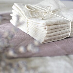 May include: A stack of white linen tea towels tied together with twine. The towels are folded and arranged neatly on a light brown surface.