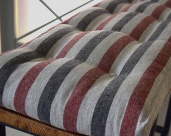 May include: A striped cushion with red, gray, and white stripes. The cushion is tufted and has a linen-like texture.