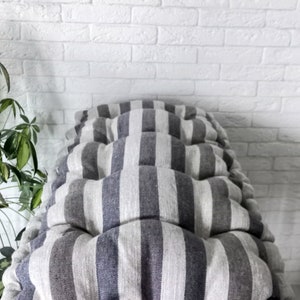 May include: A striped cushion with gray and white stripes, made of linen fabric. The cushion is sitting on a wooden bench.
