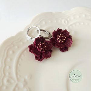 May include: A pair of burgundy crocheted flower earrings with gold accents hanging from silver hoop earrings.