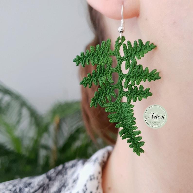 May include: Green crocheted fern earrings with silver hooks. The earrings are handmade and feature a delicate, intricate design.