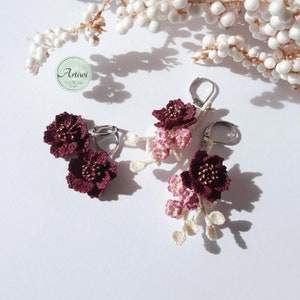 May include: A pair of burgundy crocheted flower earrings with delicate white crocheted accents hanging from silver hooks.