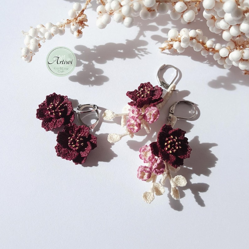 May include: A pair of burgundy crocheted flower earrings with delicate white crocheted accents hanging from silver hooks.