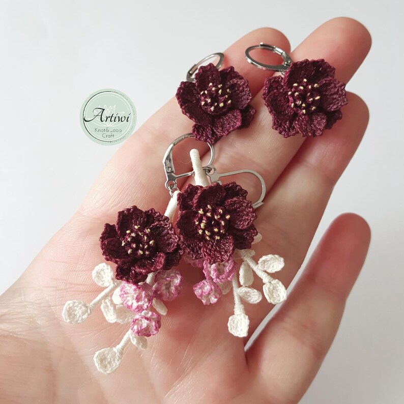 May include: A pair of crocheted flower earrings with a burgundy flower and white and pink crocheted accents.