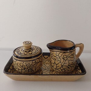 May include: A ceramic sugar and creamer set with a floral design in black on a beige background. The set is on a matching tray.