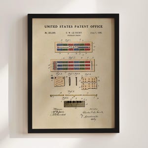 Op de afbeelding: Ingelijste patentillustratie van een cribbagebord, gedateerd 7 juli 1885, van het United States Patent Office. De tekening toont gedetailleerde weergaven van het ontwerp van het bord, inclusief pennen. Het frame is zwart.