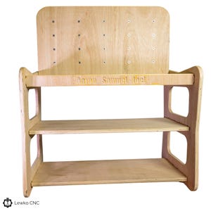 May include: A wooden shelf unit with three shelves and a back panel. The back panel has a pegboard design and is personalized with the names "Aaron, Samuel, Joel".