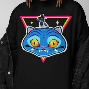 May include: Black crew neck t-shirt featuring a blue cartoon cat face with yellow eyes, pink fangs, and a hat. The cat graphic is set against a pink, yellow, and black triangle. Two white stars are on either side of the cat.