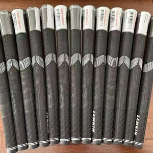 以下が含まれることがあります： 一列に並べられた13本の黒いラムキン製ゴルフクラブグリップのセット。各グリップは、上部に白い波模様のテクスチャ表面があり、Made in Mexicoと書かれた白いラベルが付いています。ブランド名のLamkinが白でプリントされています。