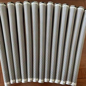 Puede incluir: Un conjunto de trece empuñaduras de palo de golf grises y negras dispuestas en fila. Cada empuñadura cilíndrica presenta un patrón texturizado repetitivo y el nombre de la marca Lamkin impreso en blanco sobre una banda negra superior.