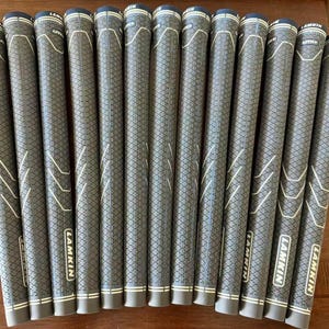 Può includere: Un set di tredici impugnature per mazze da golf Lamkin UTx disposte in fila. Ogni impugnatura presenta un motivo a rombi testurizzato, linee bianche di accento e il marchio Lamkin stampato in bianco su uno sfondo nero vicino alla base.