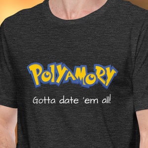 Op de afbeelding: Een donkergrijs T-shirt met een gele en blauwe afbeelding van het woord "Polyamory" in een gestileerd lettertype, vergelijkbaar met het Pokemon-logo. De tekst "Gotta date 'em all!" staat onder de afbeelding.