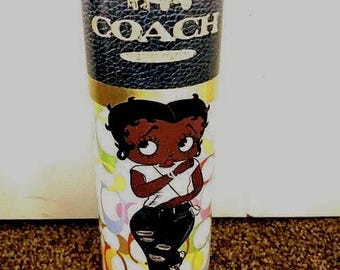 May include: A clear glass tumbler with a colourful design featuring a cartoon character. The tumbler has a gold band around the middle and the word "COACH" in gold lettering on the top.