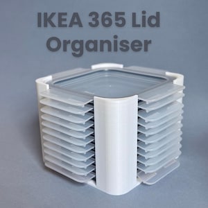 May include: White plastic IKEA 365 lid organiser with multiple slots for storage. The organiser holds clear plastic lids. The text "IKEA 365 Lid Organiser" is printed in grey.