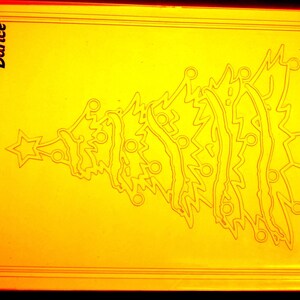 May include: A yellow Christmas tree-shaped craft with a star on top. The tree design is etched into the yellow surface. The word "Darice" is printed in the upper left corner.