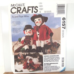 May include: McCall's Crafts 6157 sewing pattern envelope by Faye Wine featuring instructions for two white fabric snowmen figures wearing red coats, black hats, and scarves, plus gingerbread man ornaments in a basket and on a sled.