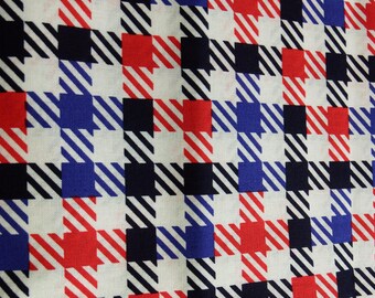 May include: Close-up of a fabric with a repeating pattern of squares in red, white, blue, and black. The squares are a mix of solid colors and diagonal stripes, creating a checkered design. The fabric appears to be cotton.