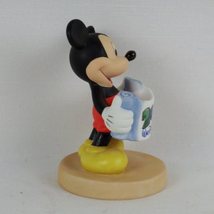 K&ouml;nnte beinhalten: Eine Keramikfigur von Mickey Mouse, die eine blaue und wei&szlig;e Schriftrolle mit dem Text "20th Anniversary Walt Disney World" h&auml;lt. Mickey tr&auml;gt seine charakteristischen roten Shorts und gelben Schuhe.