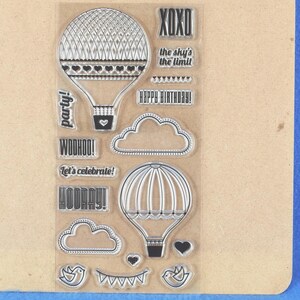 May include: Clear stamp set with hot air balloon designs, clouds, hearts, birds, and banners. Includes text: "XOXO", "the sky's the limit", "Happy Birthday!", "Party!", "Woohoo!", "Let's celebrate!", and "Hooray!"