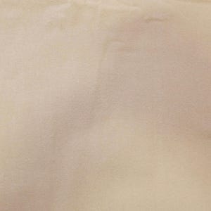 May include: A close-up shot of a beige fabric with a soft, textured appearance. The material has subtle variations in tone, creating a gentle, inviting aesthetic. The fabric appears to be smooth and possibly used for clothing or home decor.