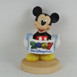 K&ouml;nnte beinhalten: Eine Keramikfigur von Mickey Mouse, die eine Schriftrolle mit dem Text "2007 Walt Disney World" h&auml;lt. Mickey tr&auml;gt seine charakteristischen roten Shorts und gelben Schuhe.