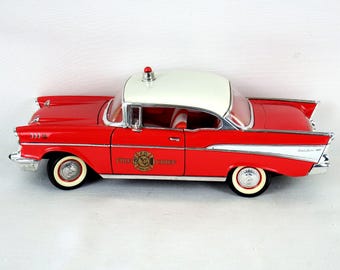 Op de afbeelding: Rood en wit vintage Chevrolet Bel Air modelauto met een brandweerchef embleem op de deur. De auto heeft whitewall banden en een rood licht op het dak.