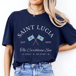 May include: A navy blue t-shirt with a white graphic design featuring the text "SAINT LUCIA" with two crossed flags and the text "EST 1979 The Caribbean Sea 13.9094° N, 60.9789° W".