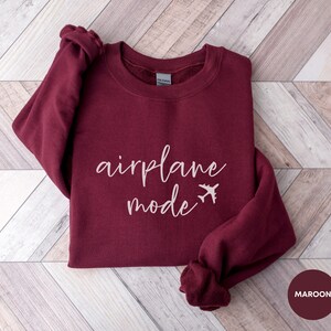 May include: A maroon sweatshirt with the text "airplane mode" in white script with a small airplane icon next to the word "mode".